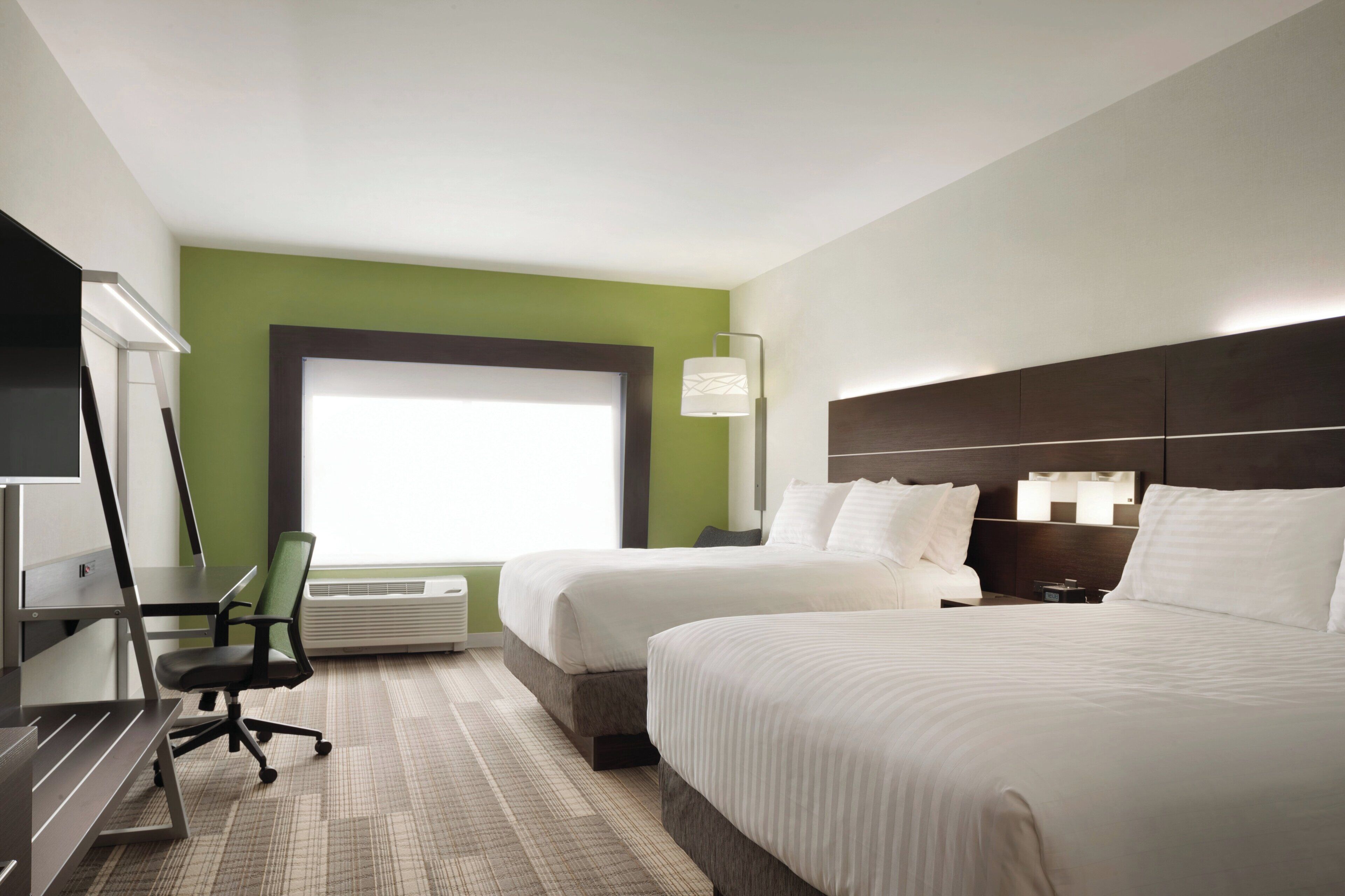 A hotel room with two beds, a desk, a chair, a TV, and a window.