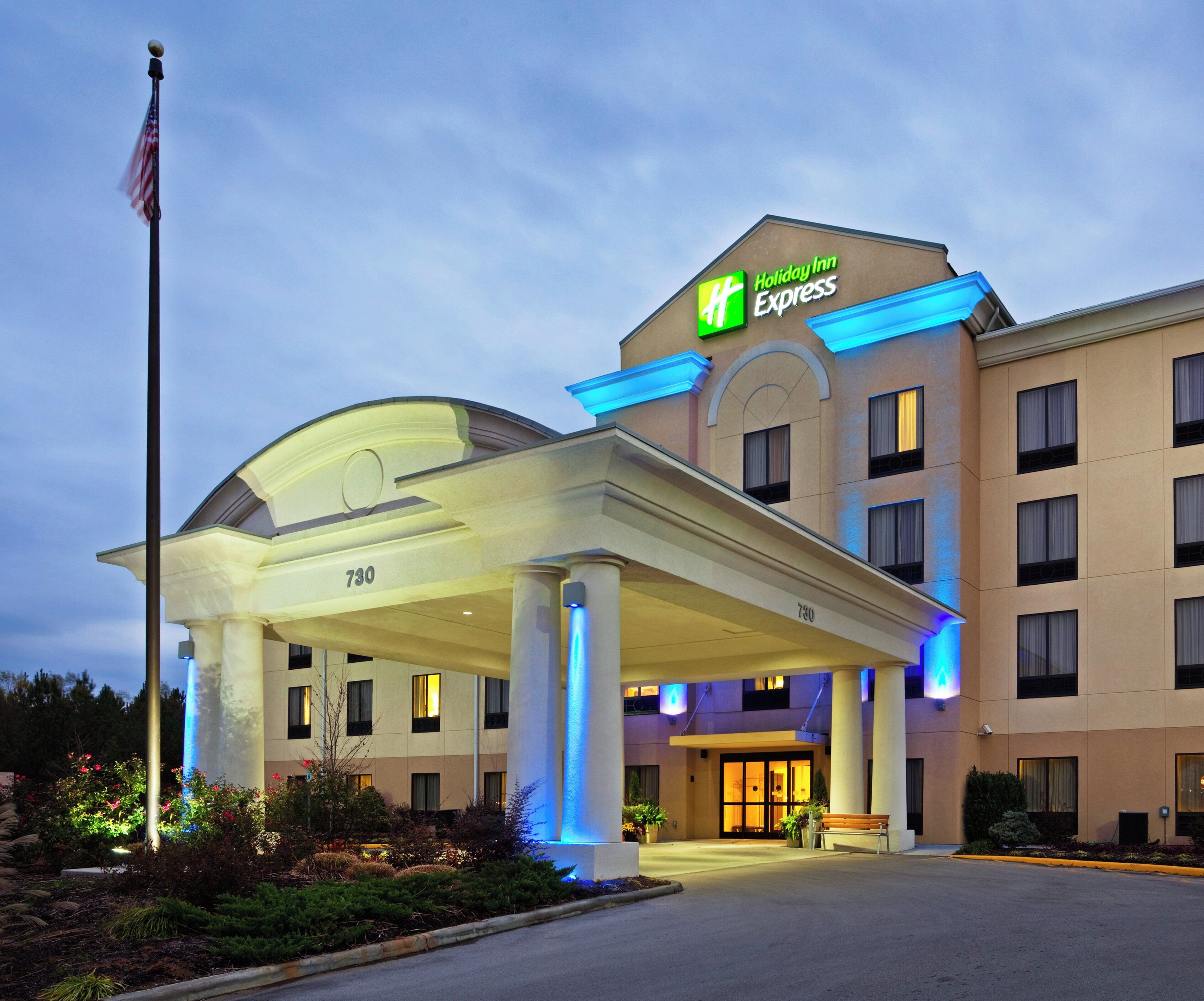Un bâtiment de l’hôtel Holiday Inn Express doté d’une entrée abritée, d’un mât pour drapeau et d’une façade bien éclairée.