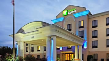 Edificio de Holiday Inn Express con entrada cubierta, asta de bandera y fachada iluminada.