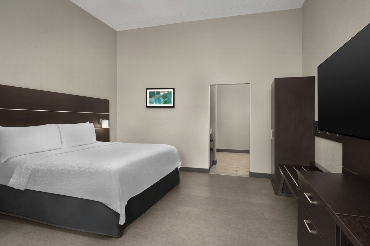 Ein Hotelzimmer mit einem Bett, einem Flachbildfernseher, einem Nachttisch und einem gerahmten Bild an der Wand.