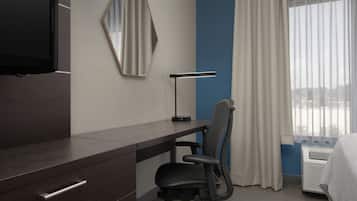 A hotel room with a desk, chair, TV, mirror, lamp, and a window with curtains.