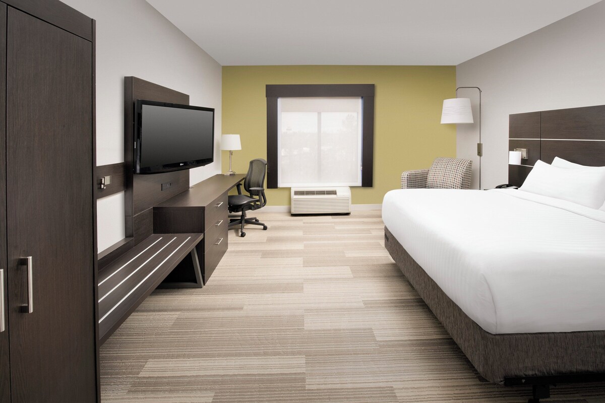 A hotel room with a bed, a desk, a chair, a television, a window, and a lamp.