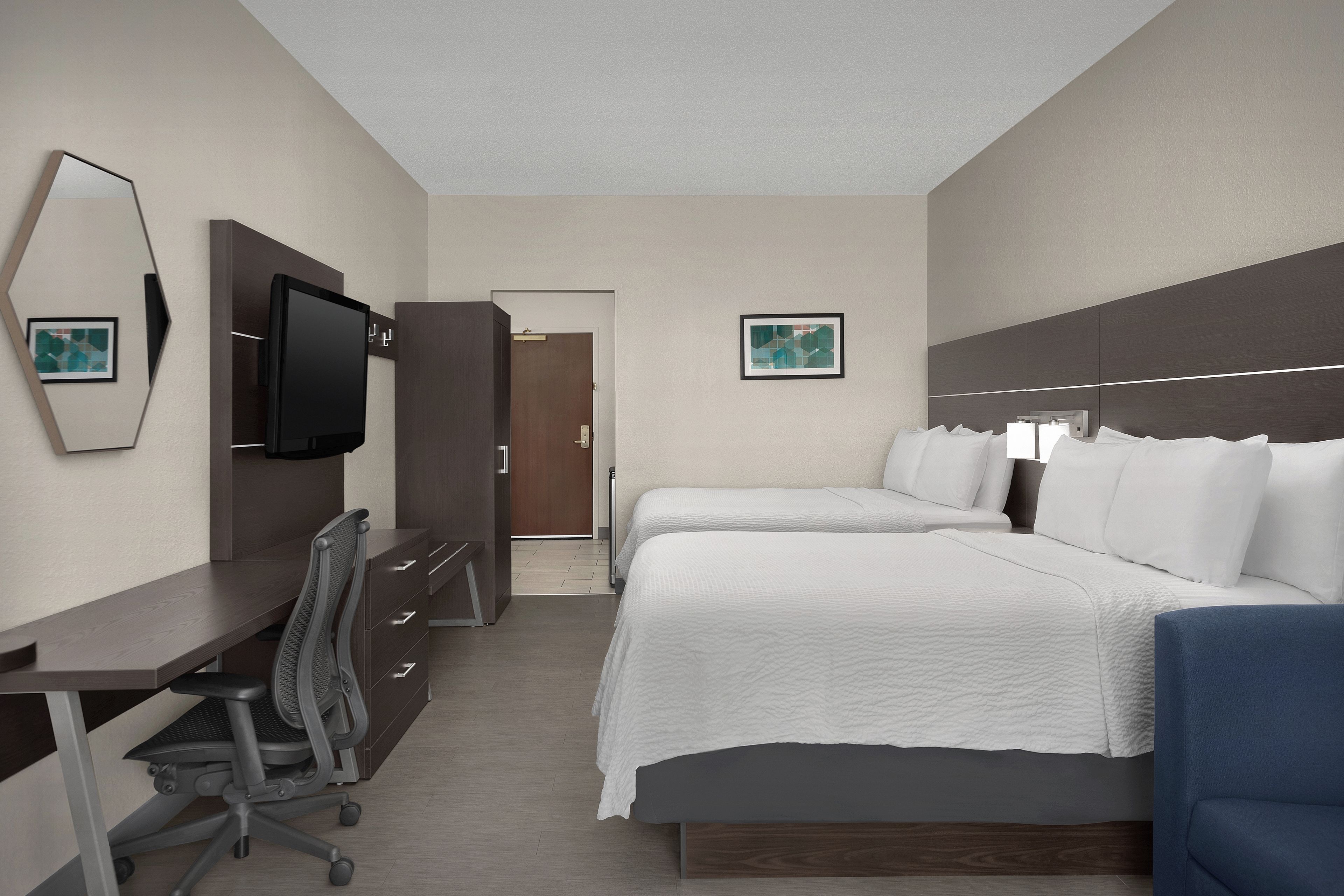 A hotel room with a bed, desk, chair, and a television.