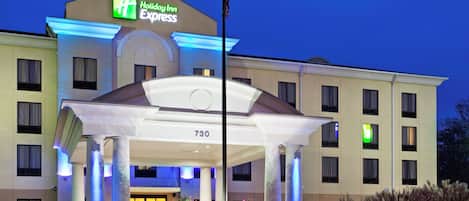 Ett Holiday Inn Express-hotell med en framträdande entré, en flaggstång och en väl upplyst fasad.