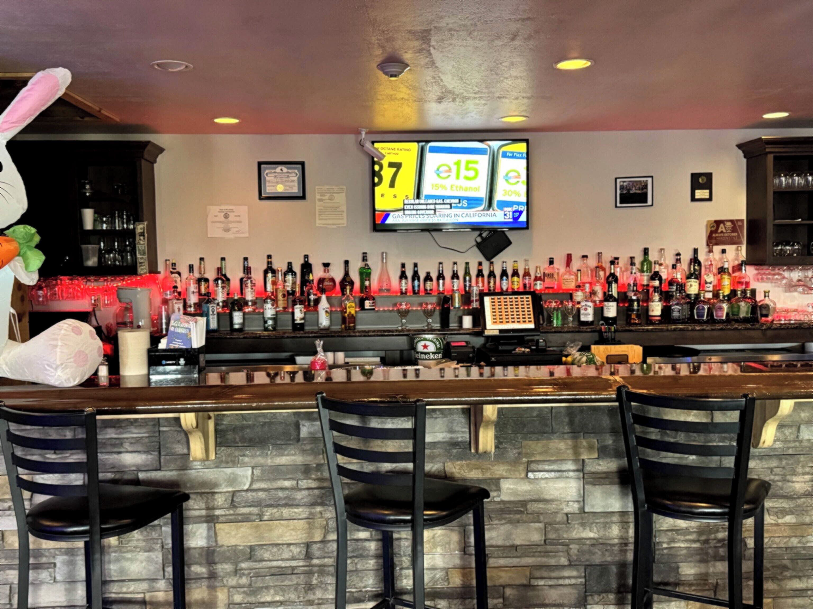 A bar area with a stone wall, multiple liquor bottles, a TV screen, and bar stools.