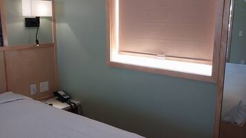 Een hotelkamer met een bed, nachtkastje, lamp en een raam met zonwering.