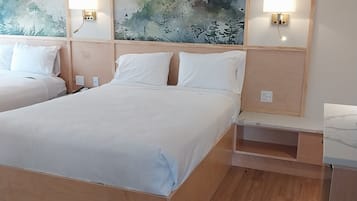 A hotel room with a large bed, a smaller bed, wooden headboard, two wall-mounted lamps, and a painting of a forest scene.