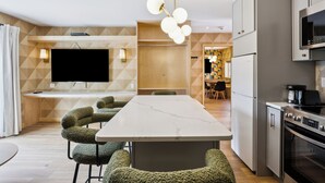Une cuisine moderne dotée d’un plan de travail en marbre, d’appareils électroménagers intégrés et d’un coin repas avec des chaises à revêtement vert.