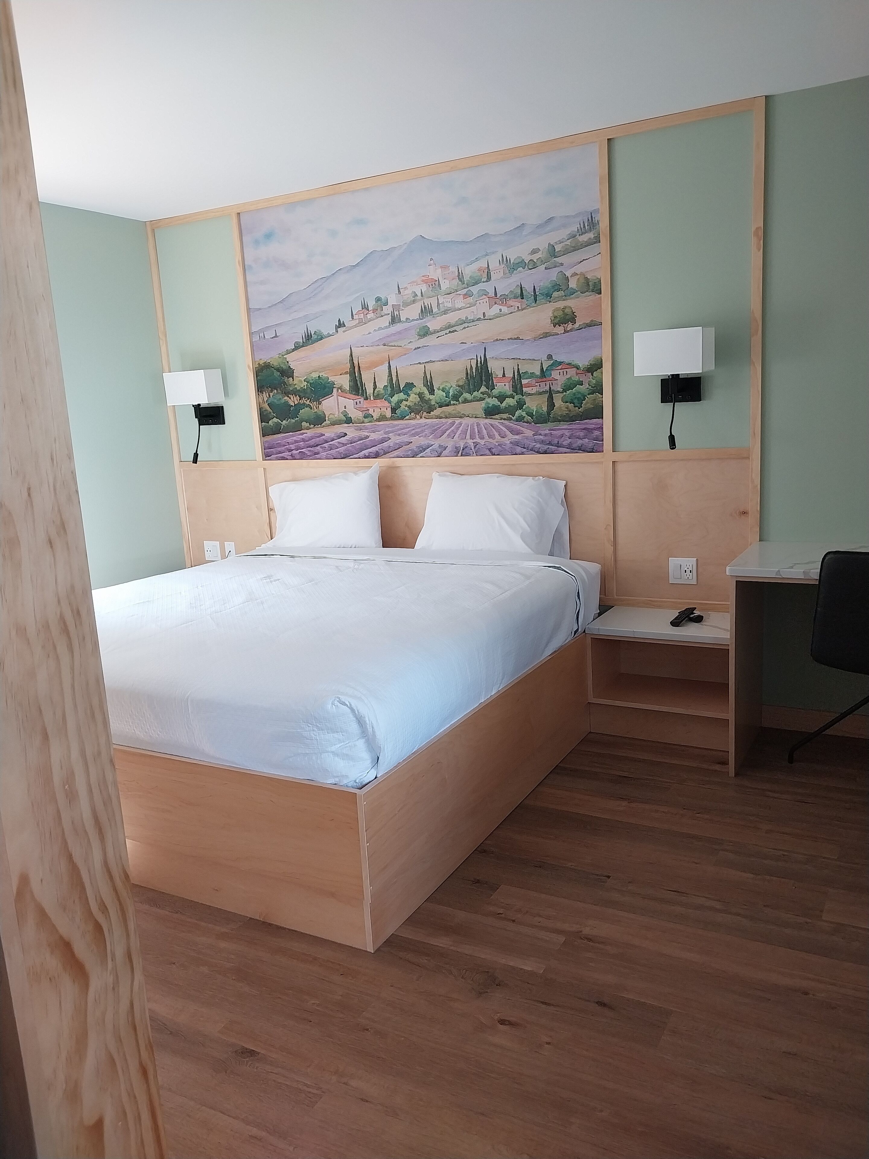 Una habitación de hotel con una cama grande, un escritorio y un cuadro de un paisaje.