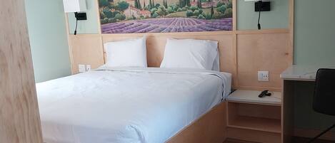 A hotel room with a large bed, a desk, and a painting of a landscape.