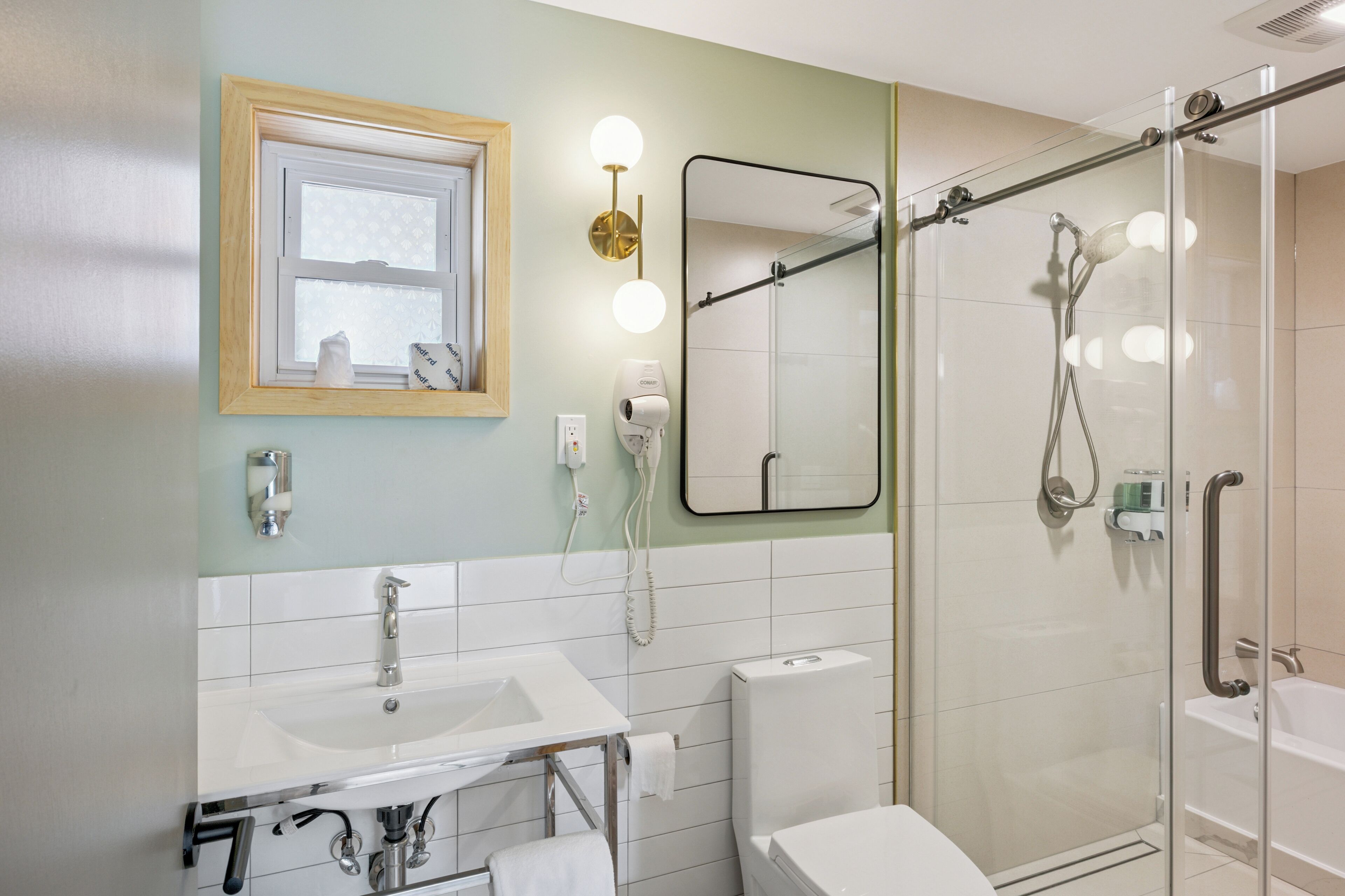 Un baño con dos lavamanos, un inodoro, una ducha con puerta de vidrio, un espejo y una ventana con persianas.