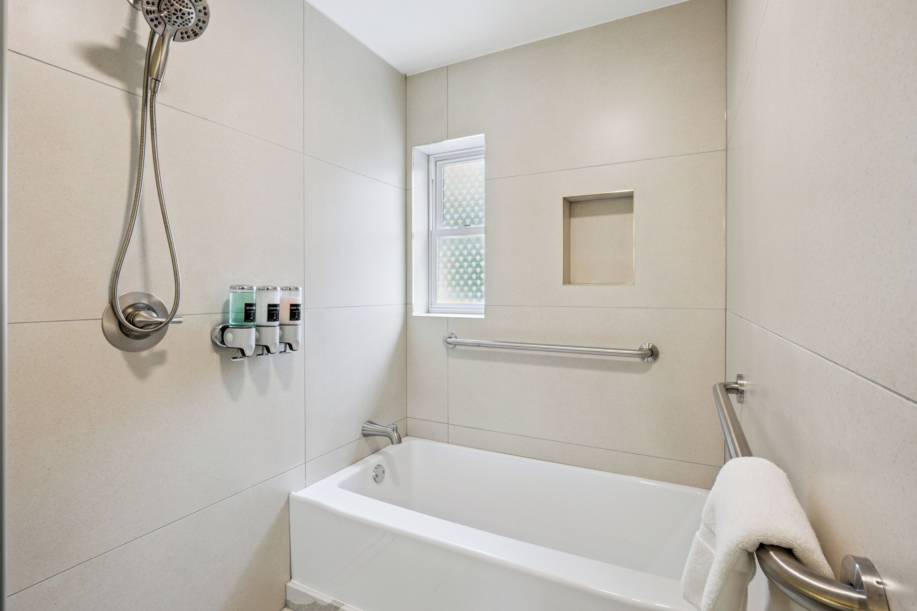 Un baño moderno con bañera, ducha de mano, ventana con diseño geométrico y toallero.