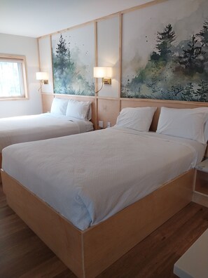 A hotel room with two single beds, wooden headboards, and a large wall mural of trees.