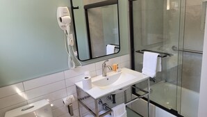 A modern bathroom with a glass shower enclosure, a white sink, and a hairdryer mounted on the wall.