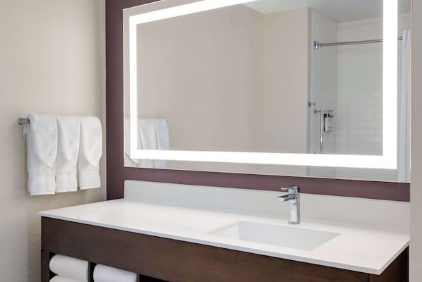 Un baño moderno con un espejo grande, lavamanos blanco y mueble de tocador oscuro.