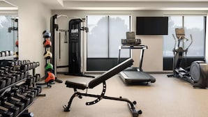 Une salle de sport équipée de bancs de musculation, d’haltères, d’un appareil à développé couché, d’un tapis de course et d’un vélo elliptique.