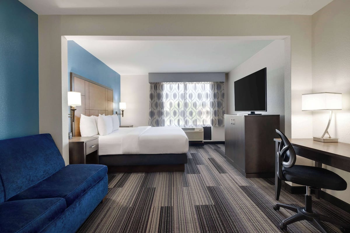 Ein Hotelzimmer mit Bett, Schreibtisch, Stuhl, Fernseher und Sofa.