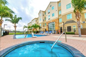 A hotel with a swimming pool, palm trees, and a brick patio.
