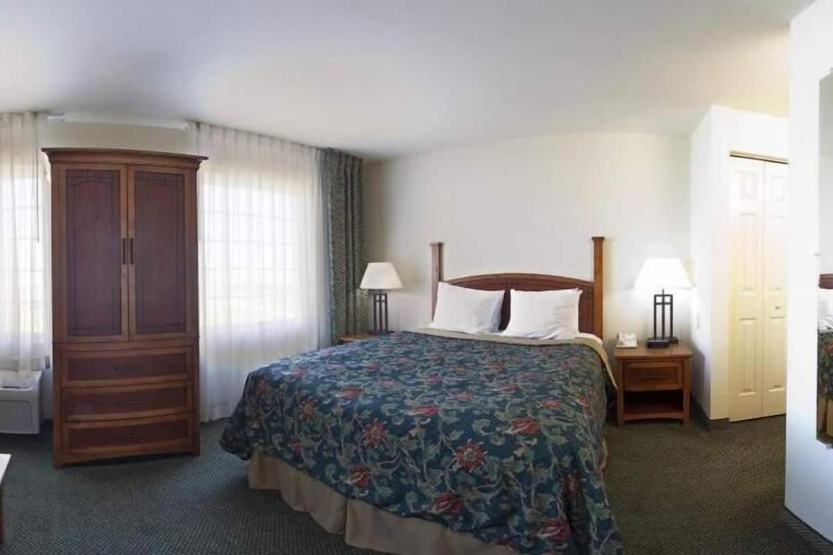 A hotel room with a large bed, a wardrobe, a desk with a lamp, and a mirror.