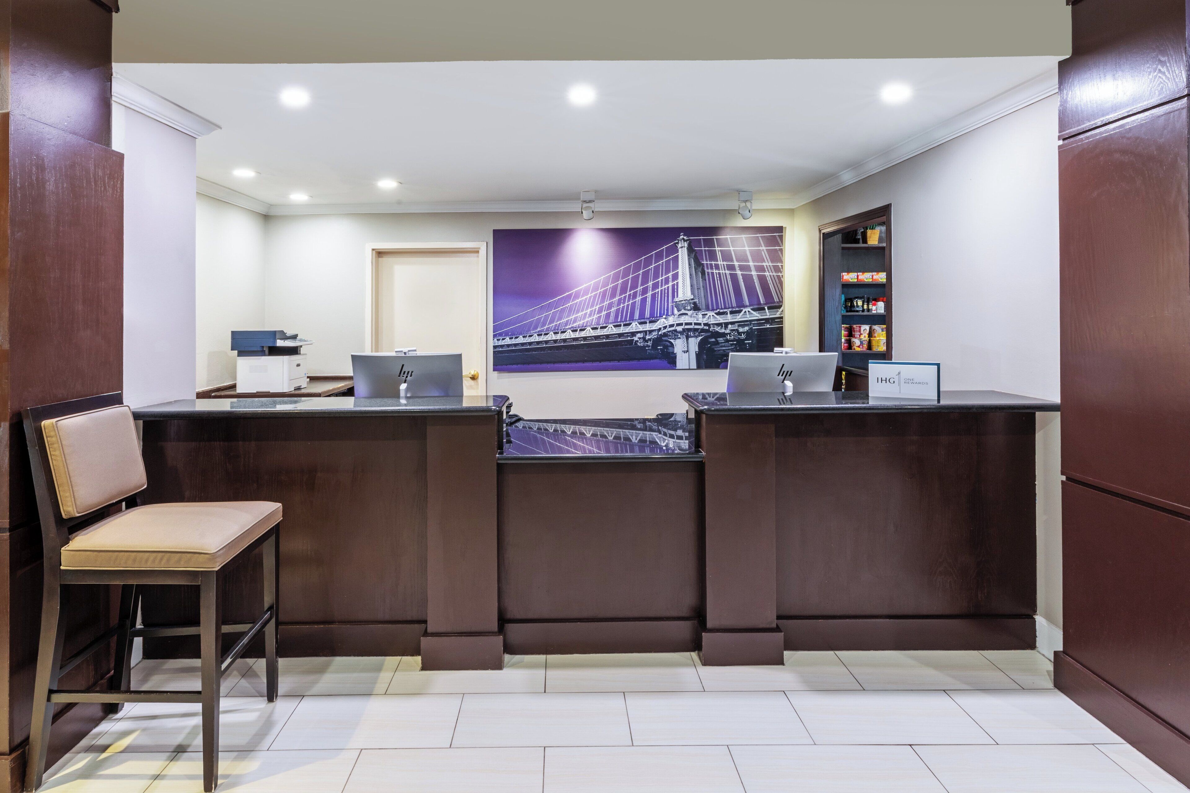 A reception desk with two computers, a chair, and a wall-mounted shelf with items.