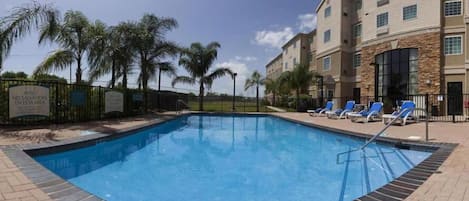 Una piscina con sillas de descanso, palmeras y un edificio de varios pisos con detalles de piedra.