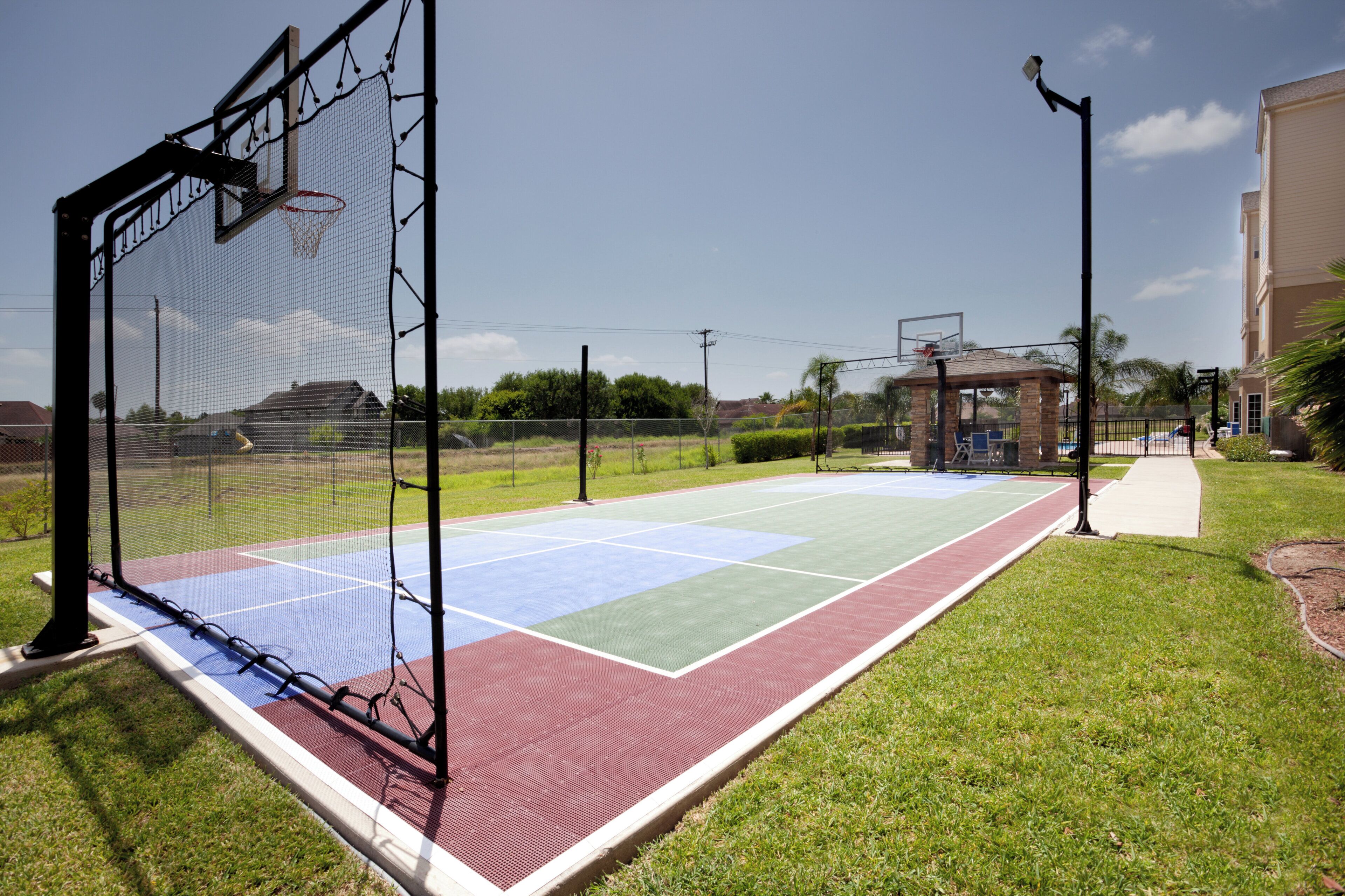 A basketball court with a net, a tennis court, and a walking path.