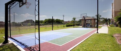 A basketball court with a net, a tennis court, and a walking path.