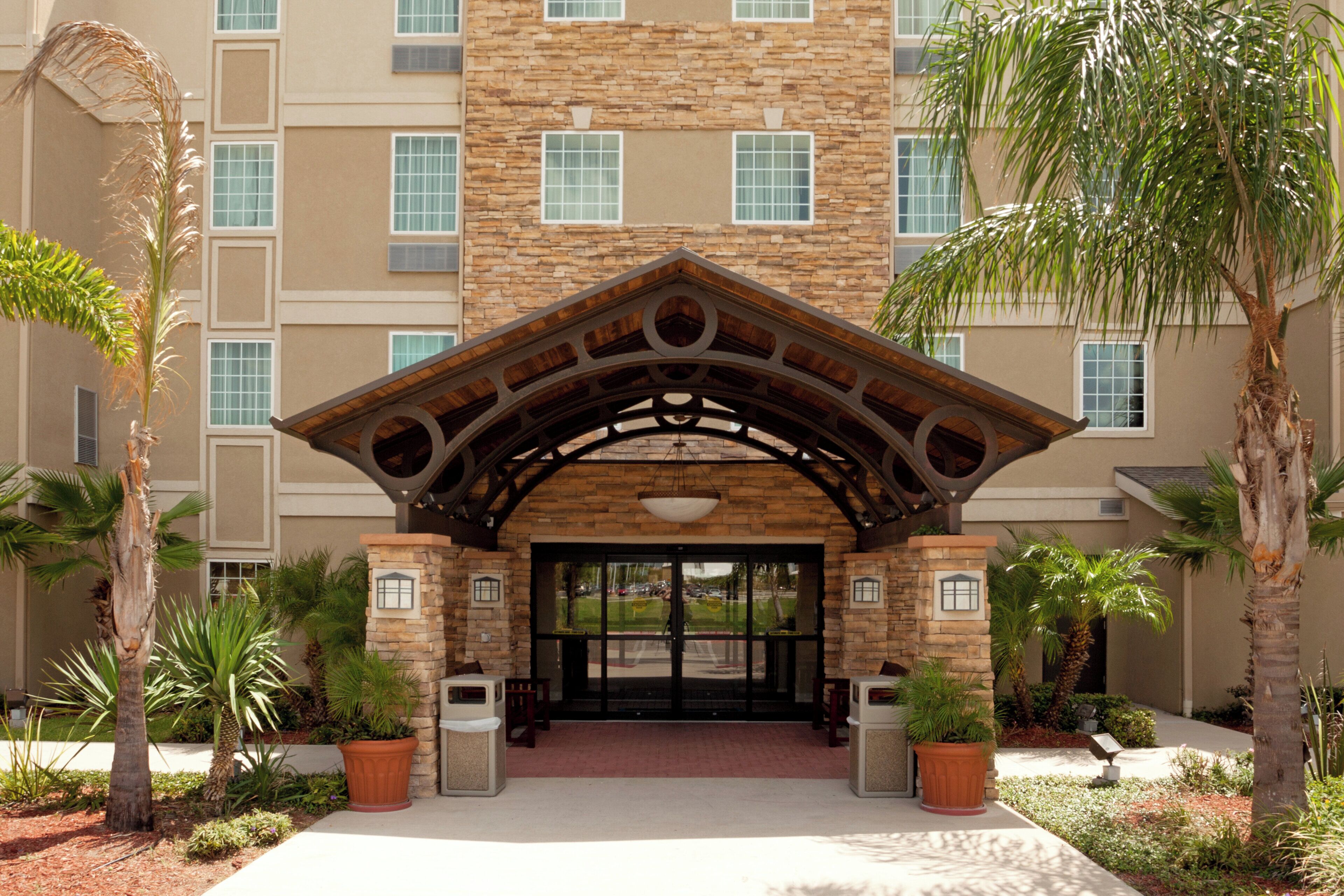 A hotel entrance with a stone facade, a wooden archway, and palm trees.