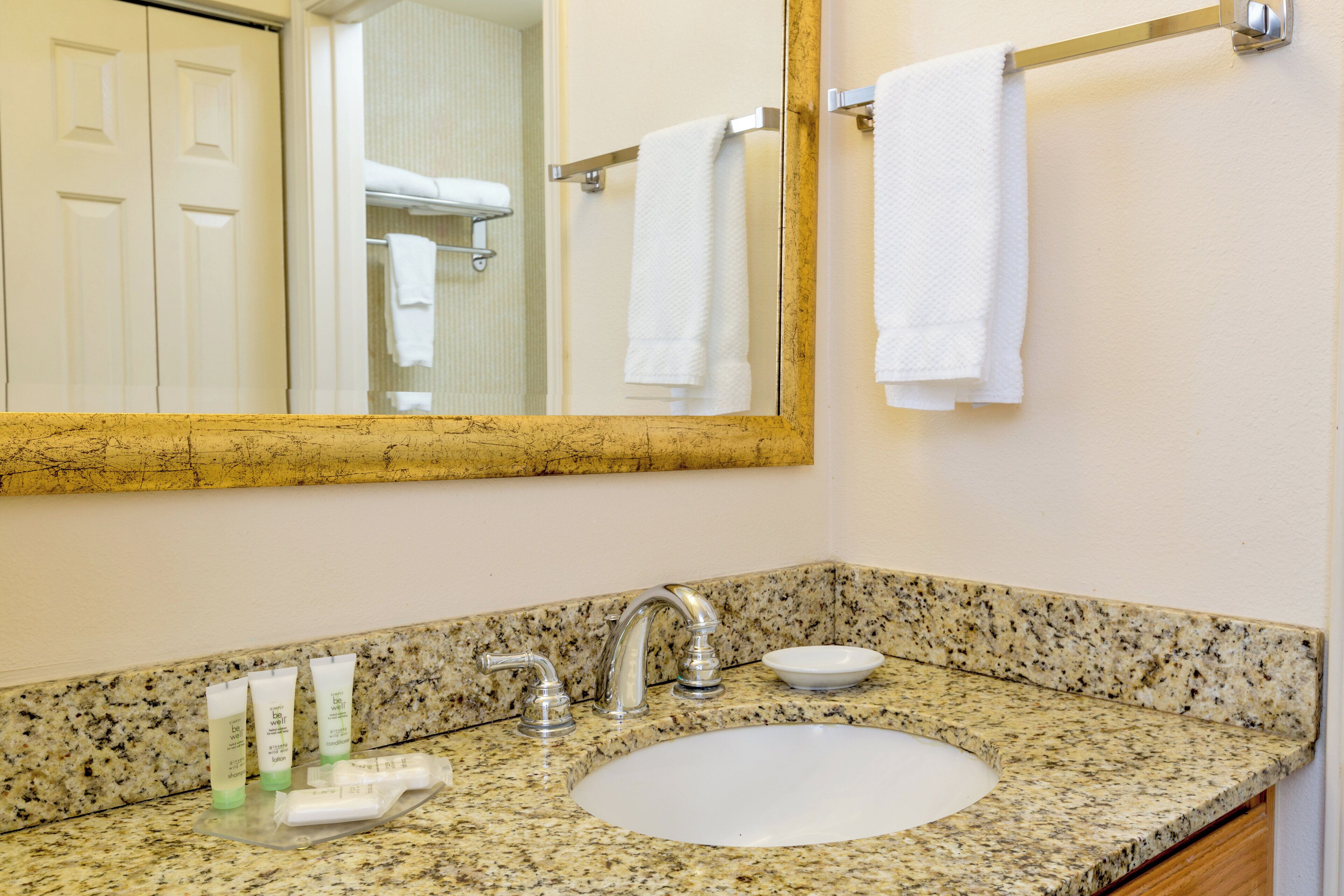A bathroom with a granite countertop, a white sink, a mirror, and a towel rack.