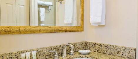 A bathroom with a granite countertop, a white sink, a mirror, and a towel rack.