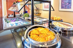 Un bufé con diversas opciones de comida, incluyendo un tazón grande de tortillas, bandejas de pastelería y una presentación de frutas.