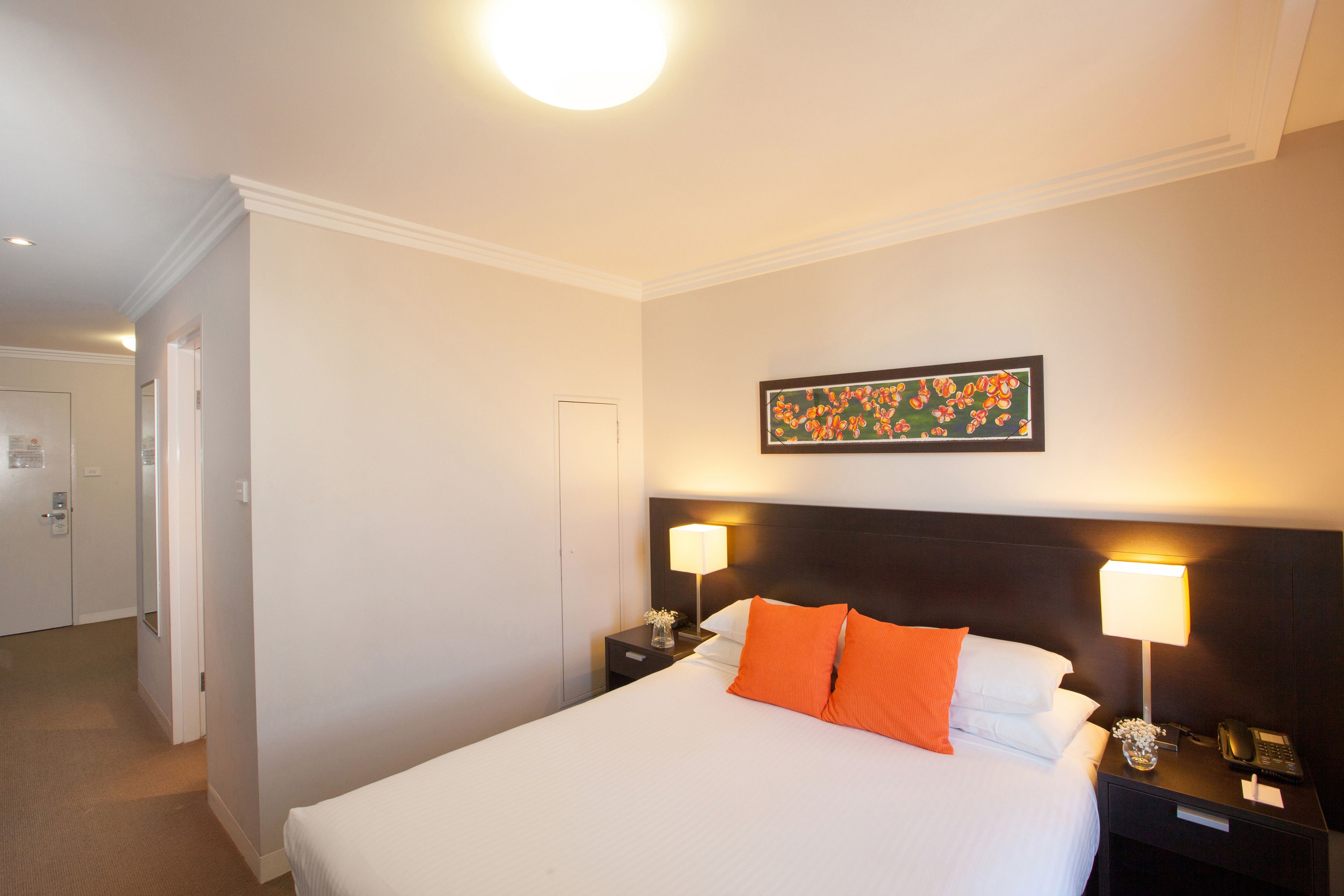 A hotel room with a large bed, two bedside tables with lamps, a framed floral artwork on the wall, and a door leading to another room.