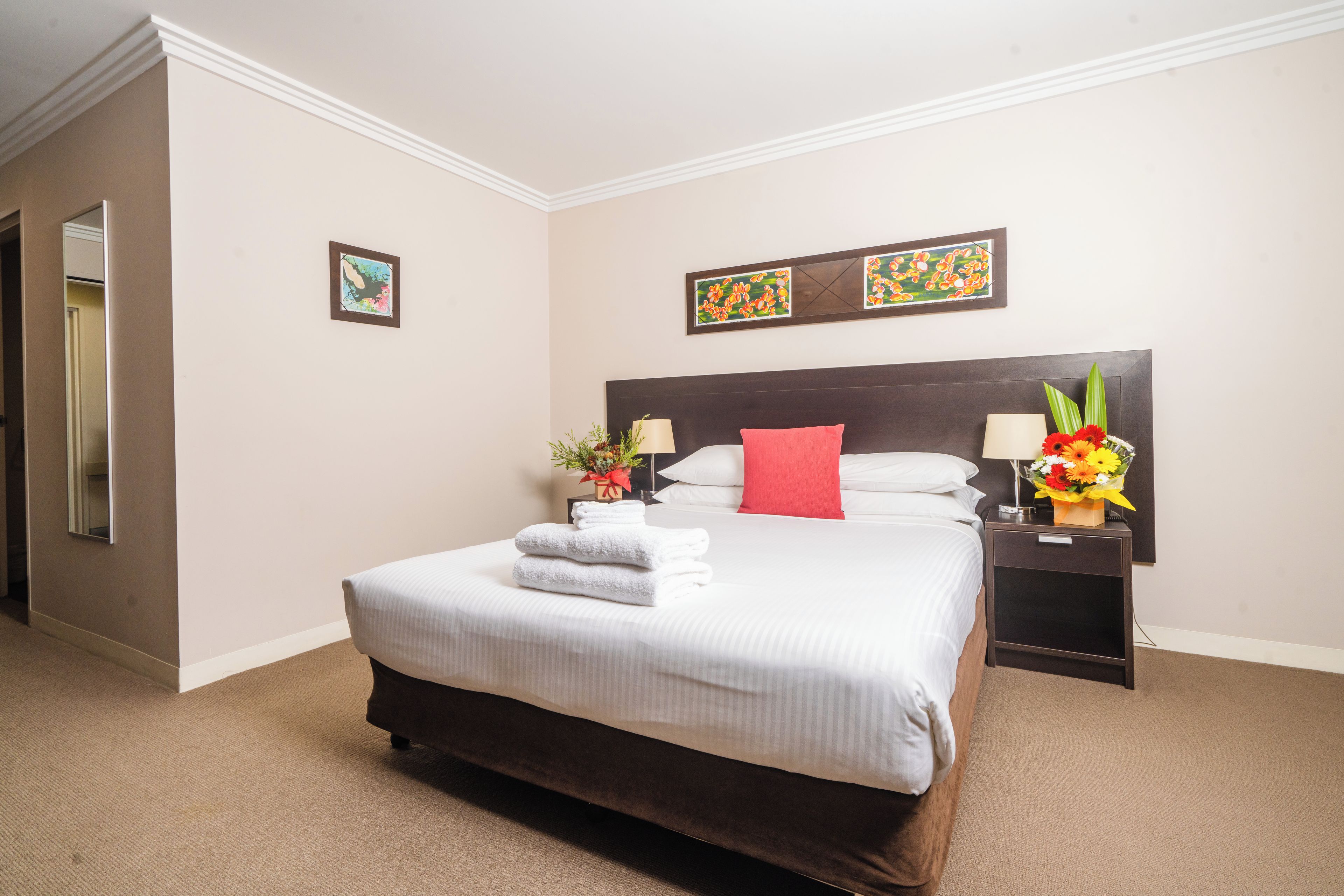 A hotel room with a large bed, a nightstand with a lamp, and two wall-mounted paintings.