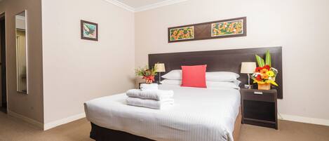 A hotel room with a large bed, a nightstand with a lamp, and two wall-mounted paintings.
