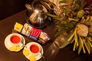A table with two cups of tea, a teapot, a tray of biscuits, and a decorative plant.