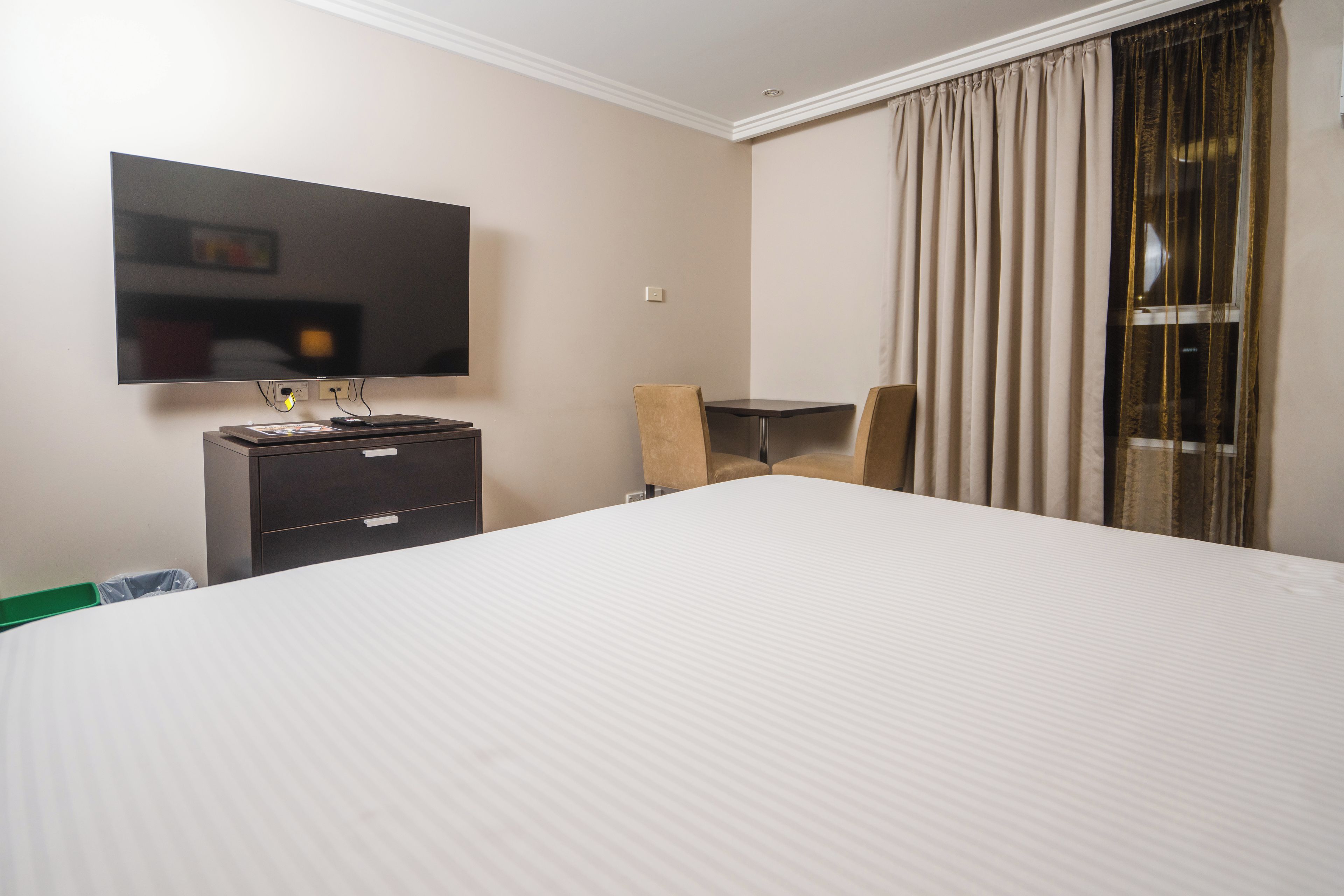 A hotel room with a large bed, a flat-screen TV mounted on the wall, a small desk, and a chair.