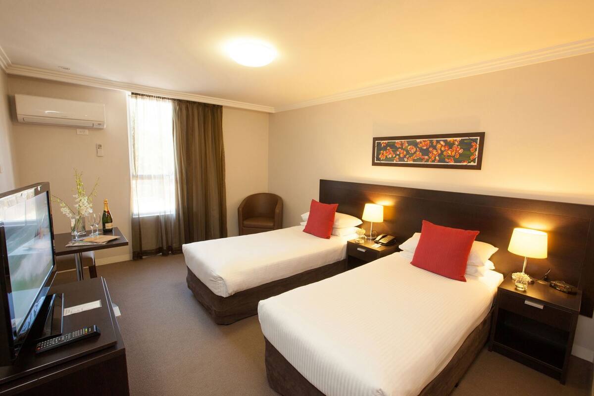 A hotel room with two beds, a TV, a desk with a remote, and a window with curtains.
