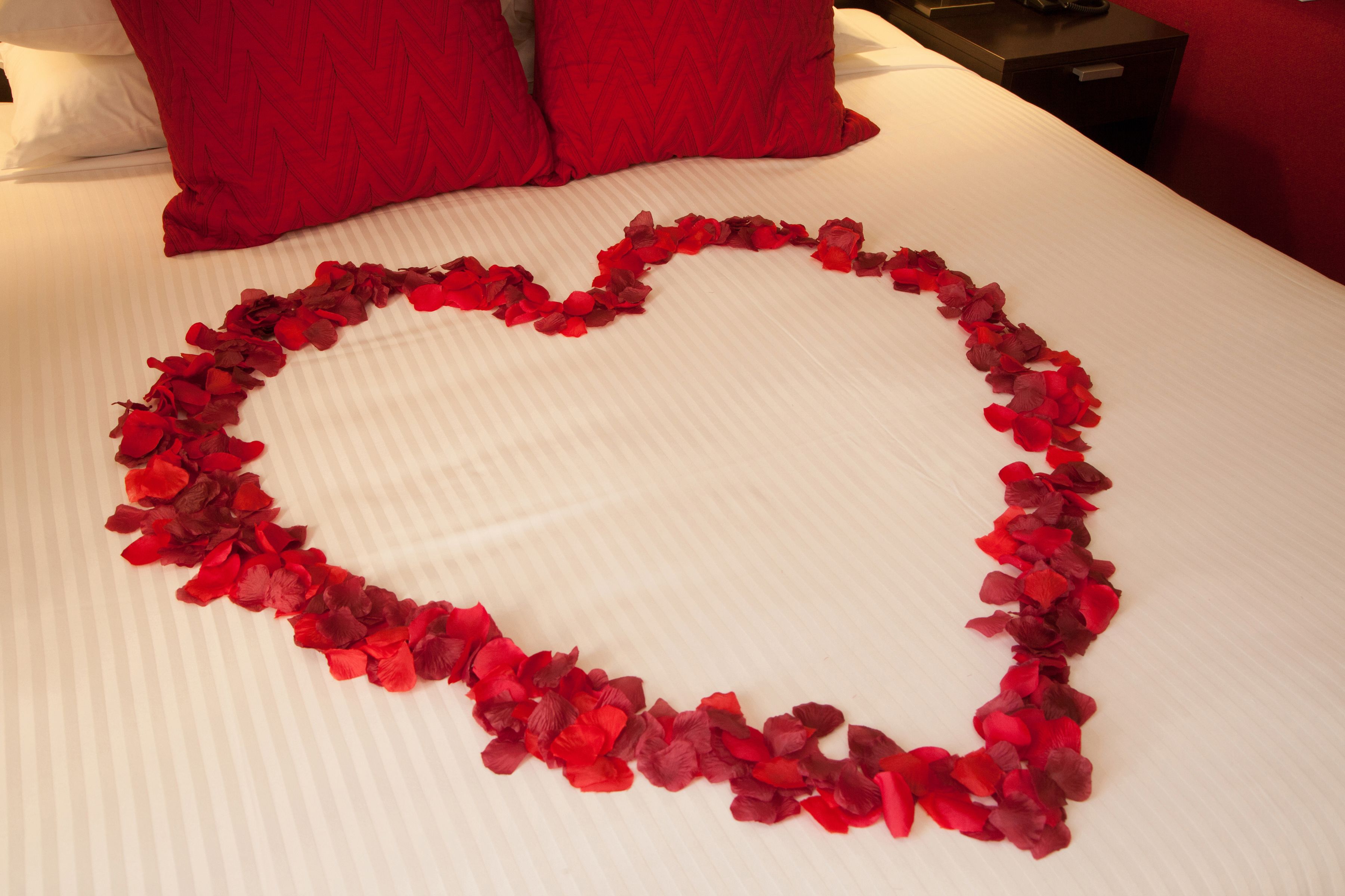Una cama con un arreglo de pétalos de rosa en forma de corazón.