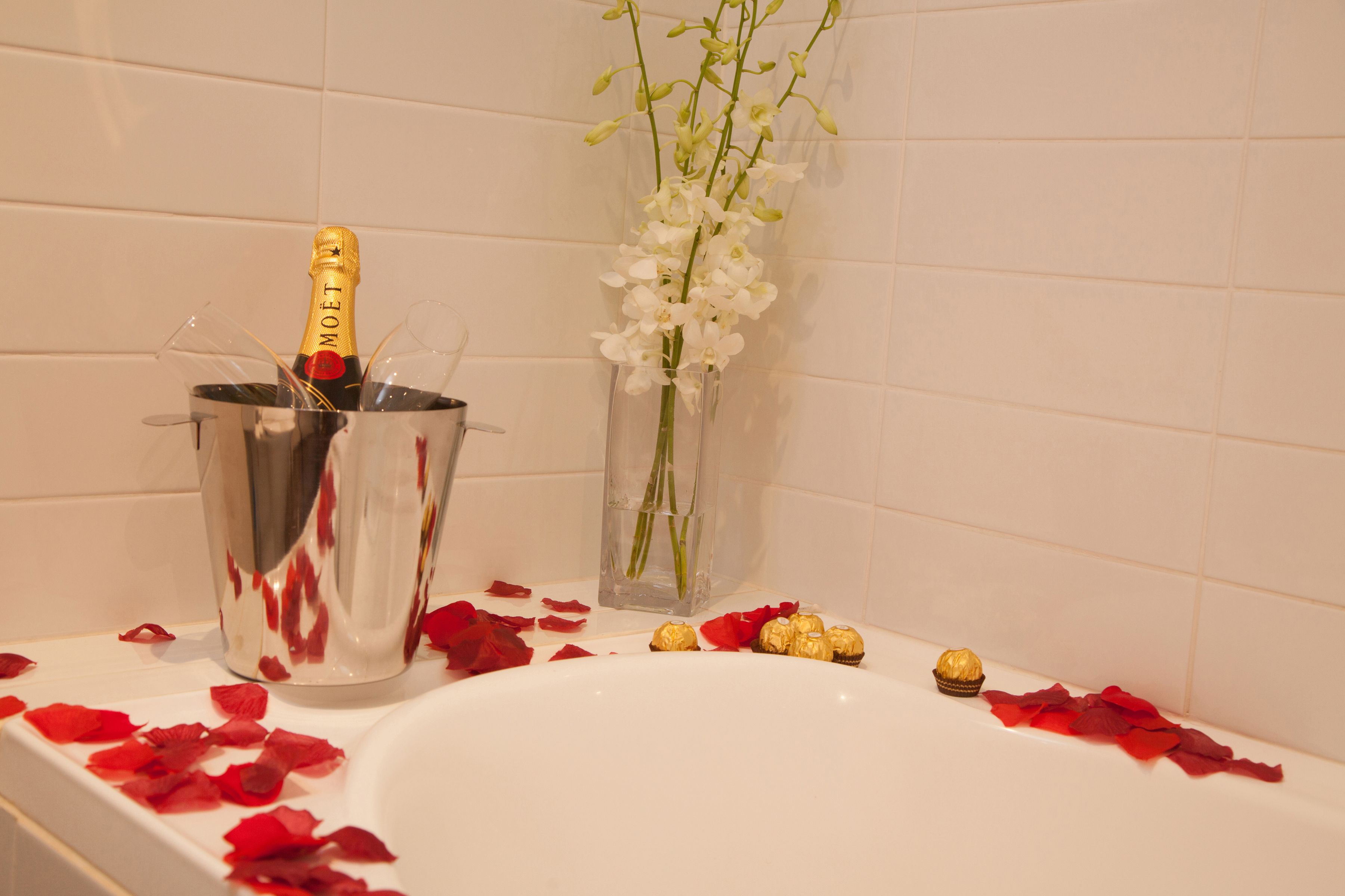 A bathtub with champagne, flowers, and rose petals.