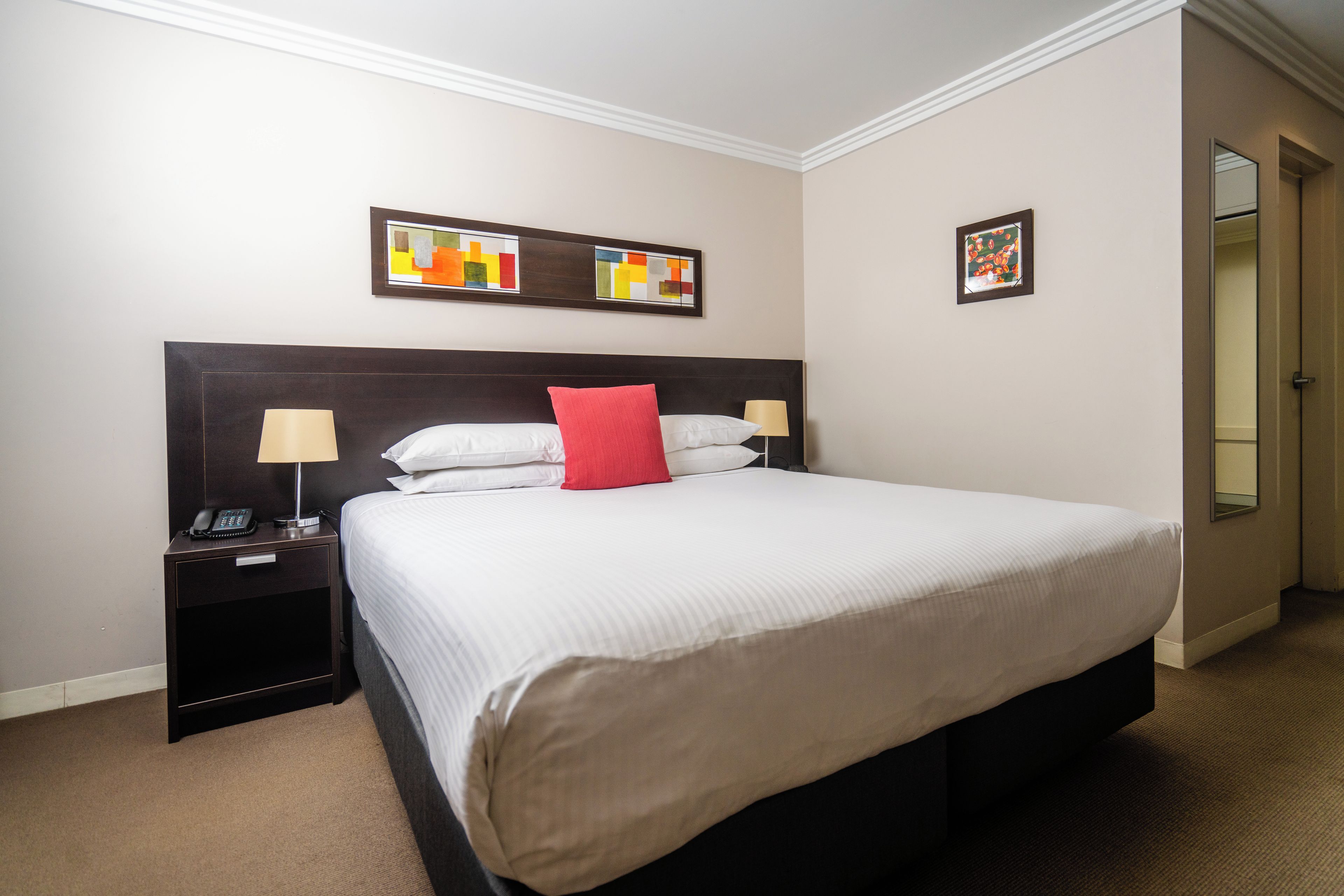 Une chambre d’hôtel avec un grand lit, deux tables de chevet avec des lampes et des œuvres d’art accrochées aux murs.
