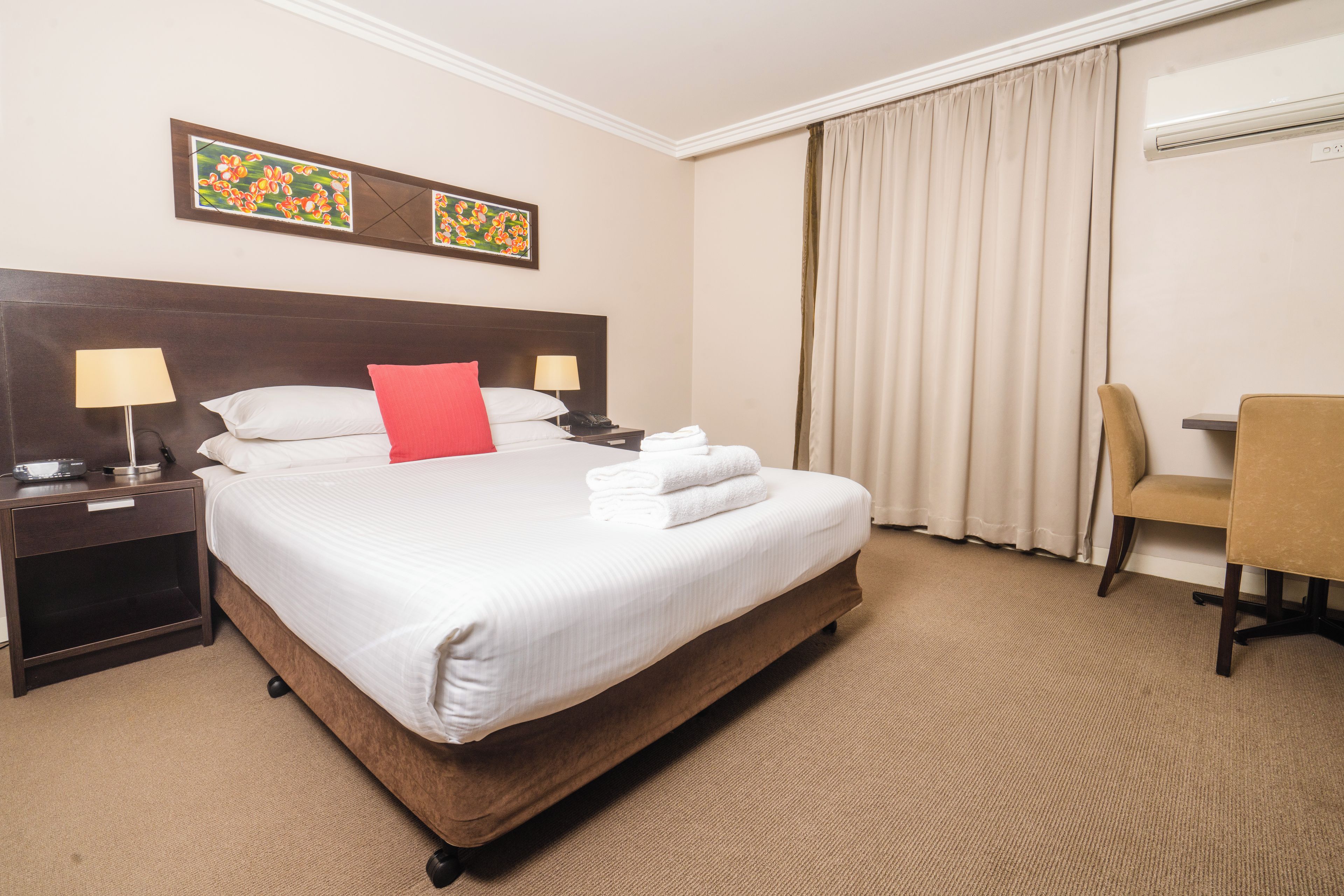 A hotel room with a large bed, two bedside tables with lamps, a chair, and a desk.