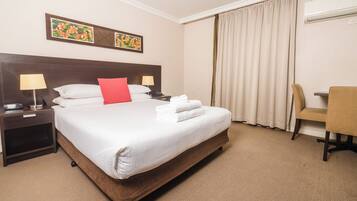 A hotel room with a large bed, two bedside tables with lamps, a chair, and a desk.