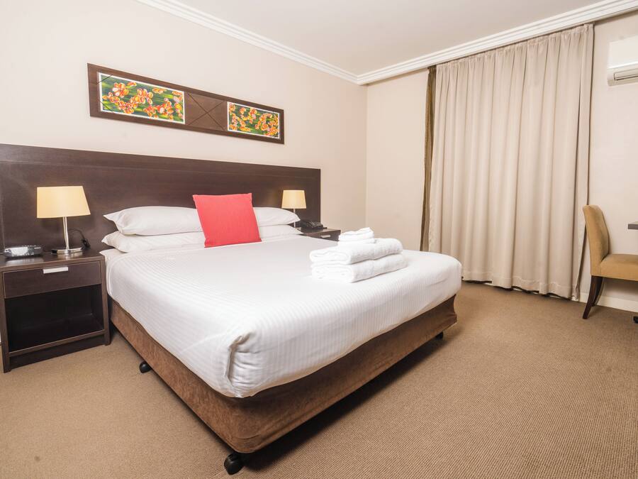 A hotel room with a large bed, two bedside tables with lamps, a chair, and a desk.