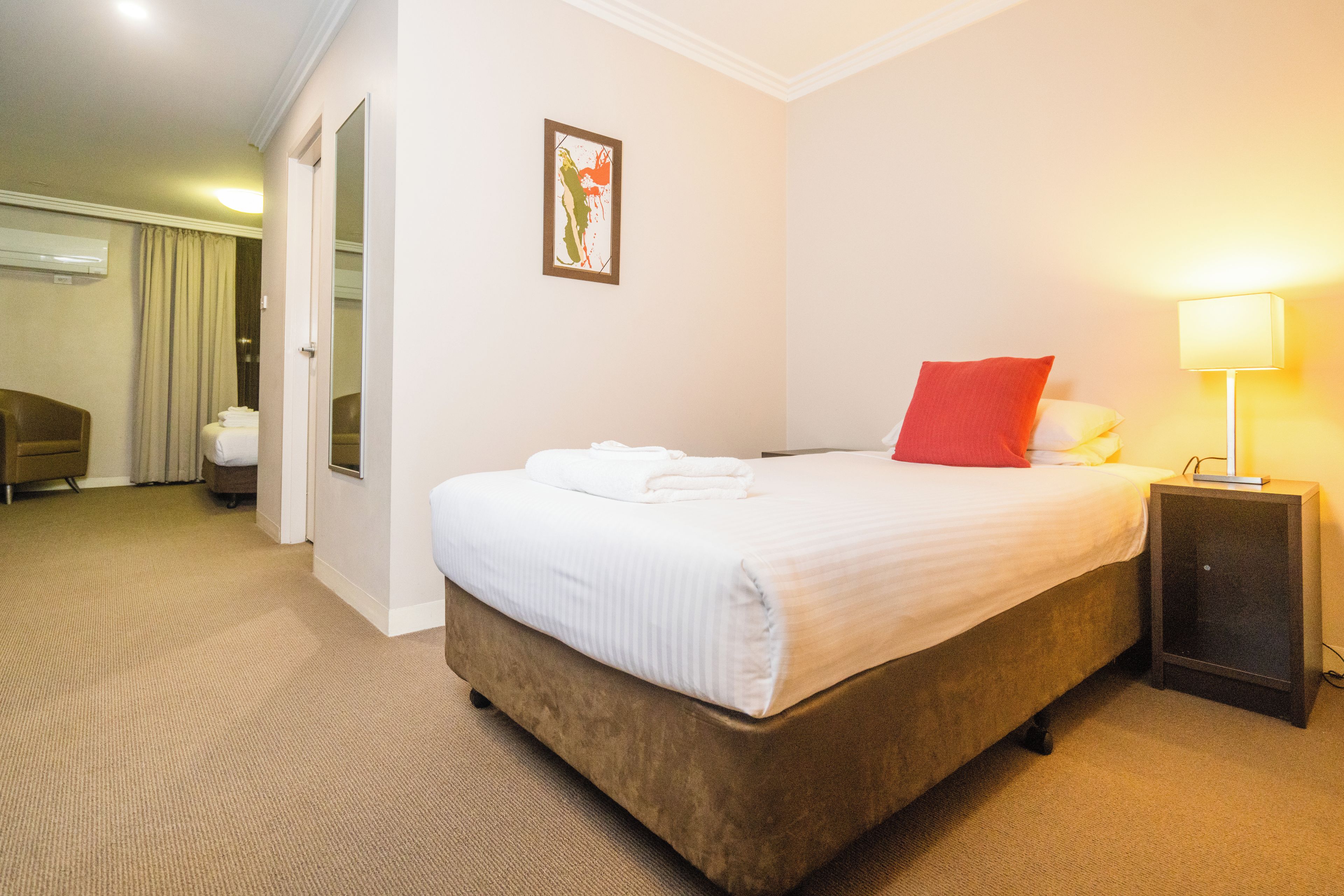 A hotel room with a bed, a bedside table with a lamp, a door leading to a bathroom, and a wall-mounted picture.