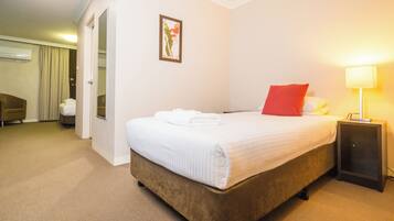 A hotel room with a bed, a bedside table with a lamp, a door leading to a bathroom, and a wall-mounted picture.
