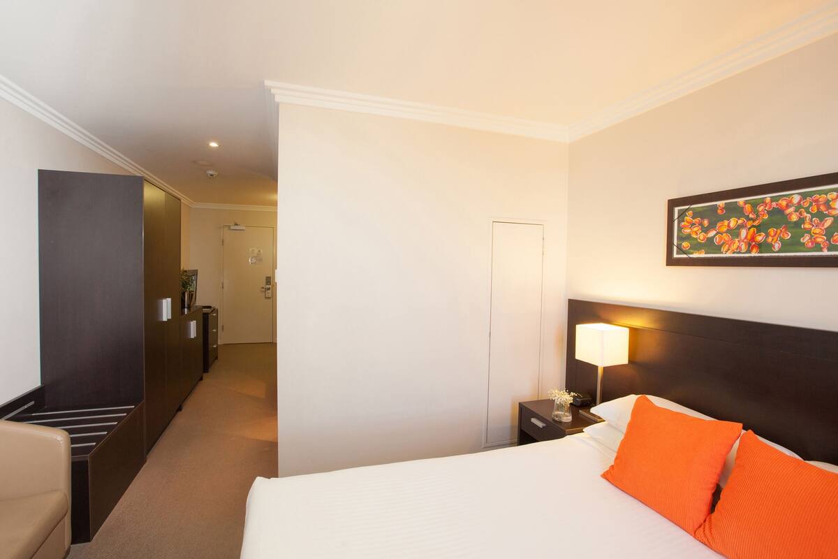 A hotel room with a bed, nightstand, lamp, and a painting on the wall.