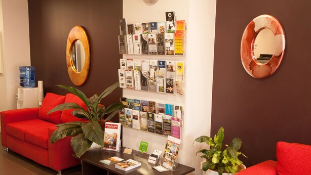 Een receptiegedeelte met een rode bank, een bijzettafeltje en een prikbord met diverse brochures.