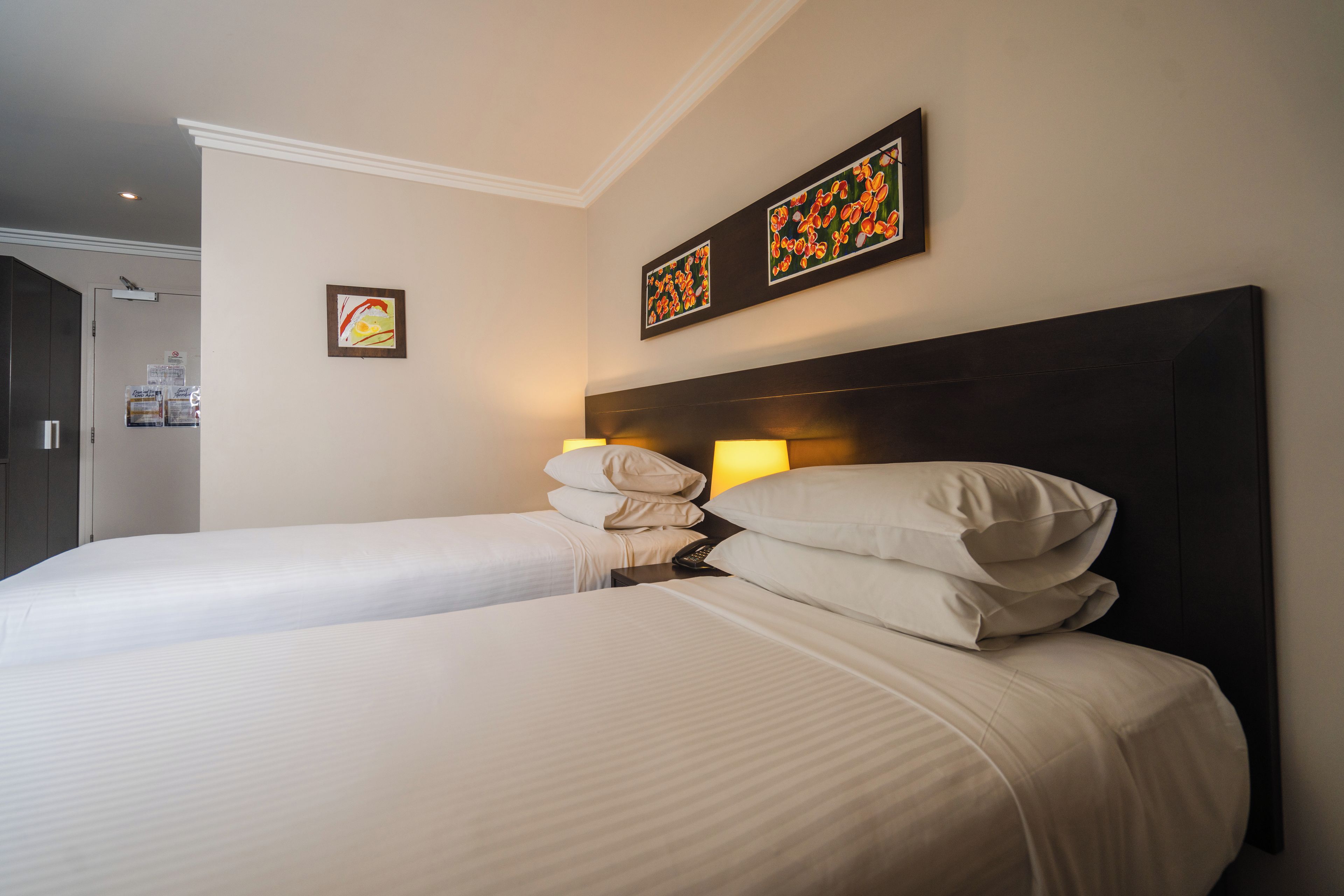 Een hotelkamer met twee bedden, een donker hoofdeinde en twee wanddecoraties.