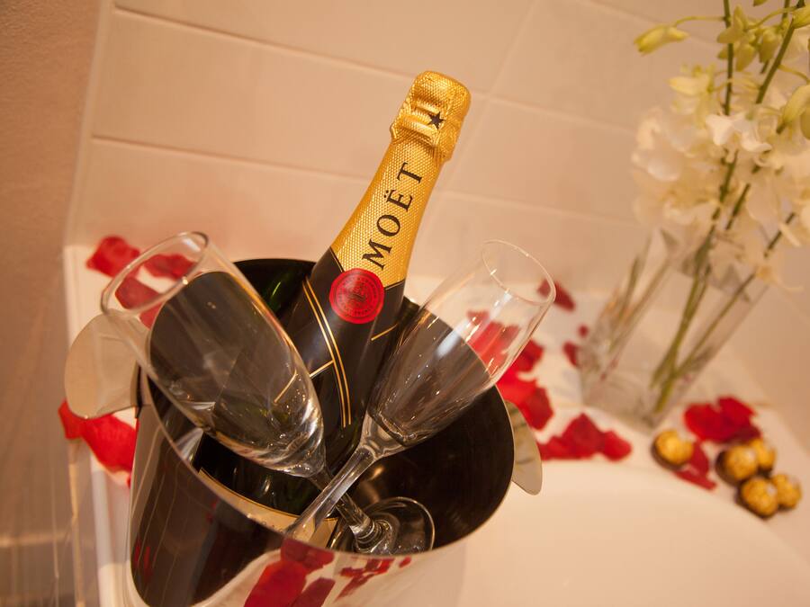 Eine Champagnerflasche mit Gläsern in einem Kübel, umgeben von Rosenblättern.