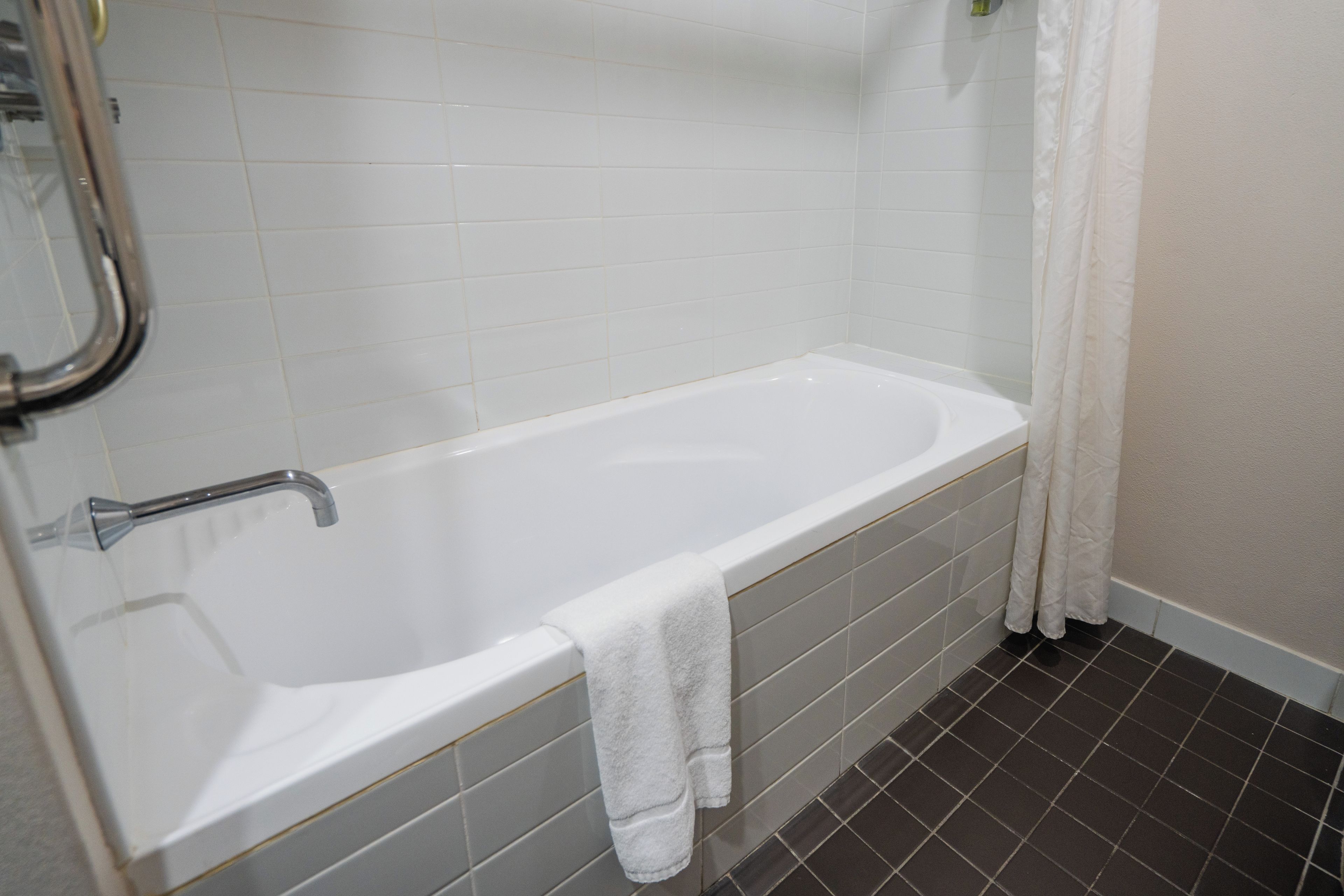 A standard white bathtub with a shower head, a towel hanging on the side, and a tiled floor.